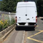 White van parked partly on a narrow pavement and partly on yellow zig zags